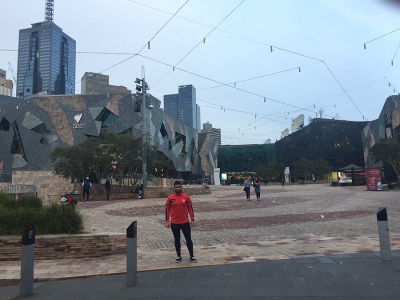 chico joven en una calle de Melbourne con cielo cubierto y los edificios a la izquierda. 